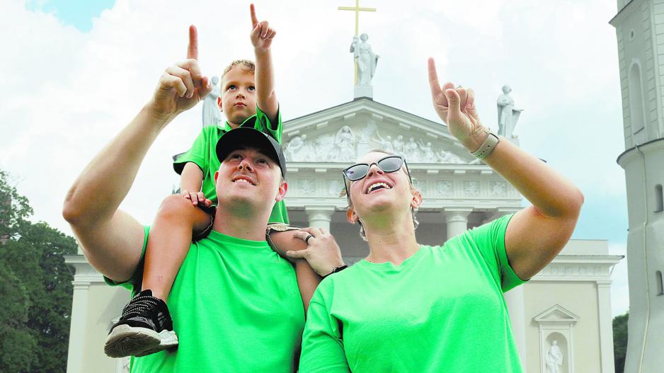 vyras, moteris ir vaikas žaliais marškinėliais rodo į dangų Vilniaus katedros fone