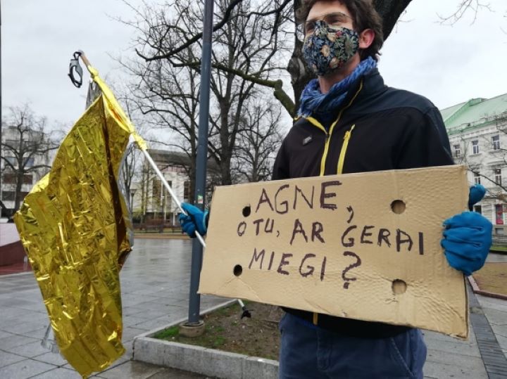 protestuotojas su auksine vėliava ir plakatu "Agne, ar tu gerai miegi?"