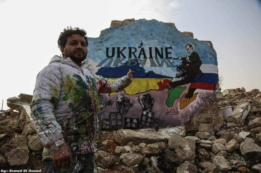 menininkas rodo grafitį, kuriame Putino puolama Ukraina