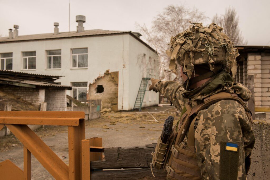 kareivis su Ukrainos uniforma pirštu rodo į skylę pastate
