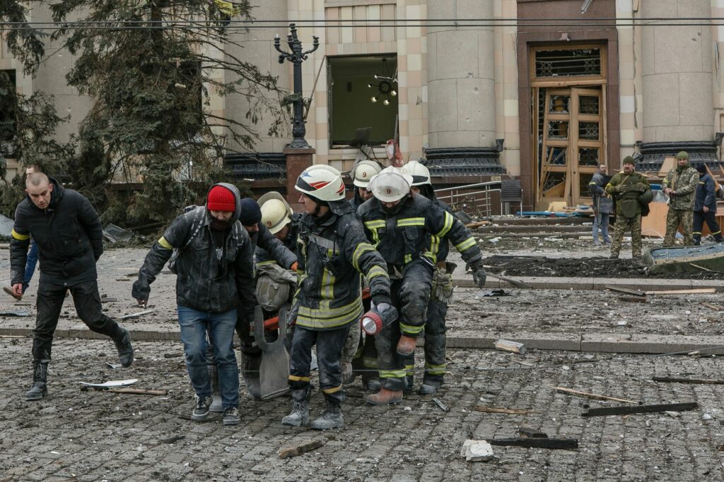 ugniagesiai neša žmogų neštuvuose iš subombarduoto namo Ukrainoje