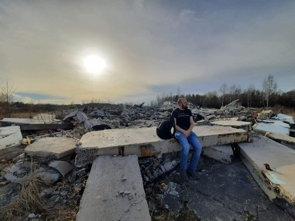 Autorius sėdi sugriauto pastato griuvėsiuose, ant betono plokštės, saulę dengia debesys. Jokio pykčio