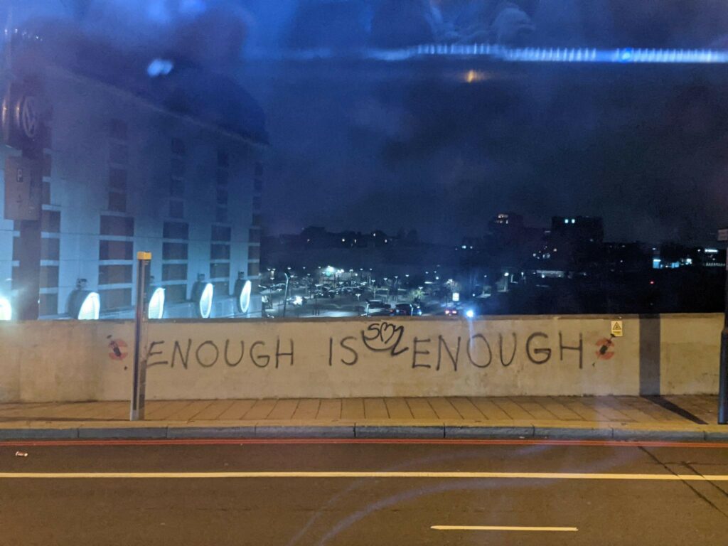 a city at night, a wall on which graffiti reads "enough is enough"
