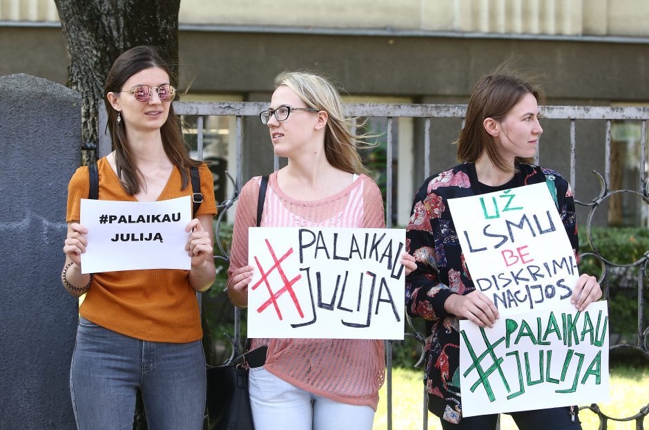 Trys merginos su plakatais "Palaikau Juliją" prie Lietuvos sveikatos mokslų universiteto