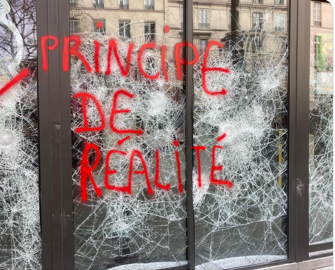 protestai Prancūzijoje: ant sudaužyto lango raudonai parašyta "Tikrovės principas"