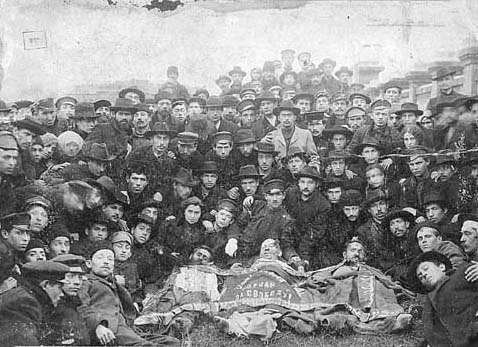 Daug Bundo narių susirinkę prie trijų žuvusių bendražygių kūnų. Nespalvota 1905 metų nuotrauka