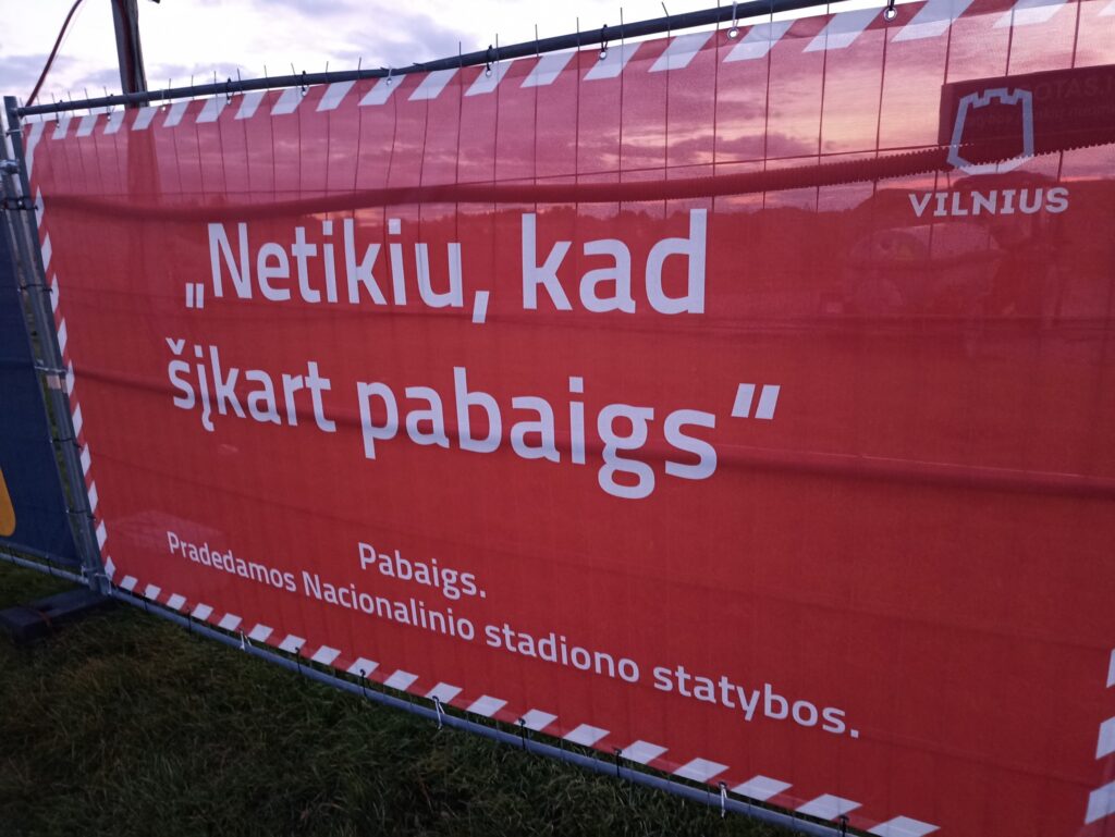 Reklama ant vielinės statomo Nacionalinio stadiono tvoros: „Netikiu, kad šįkart pabaigs“. Apačioje parašyta: „Pabaigs. Pradedamos Nacionalinio stadiono statybos.“