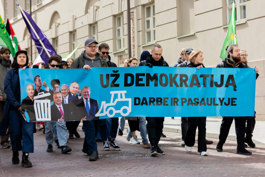 Žmonės neša žydrą transparantą su šūkiu „Už demokratiją darbe ir pasaulyje“