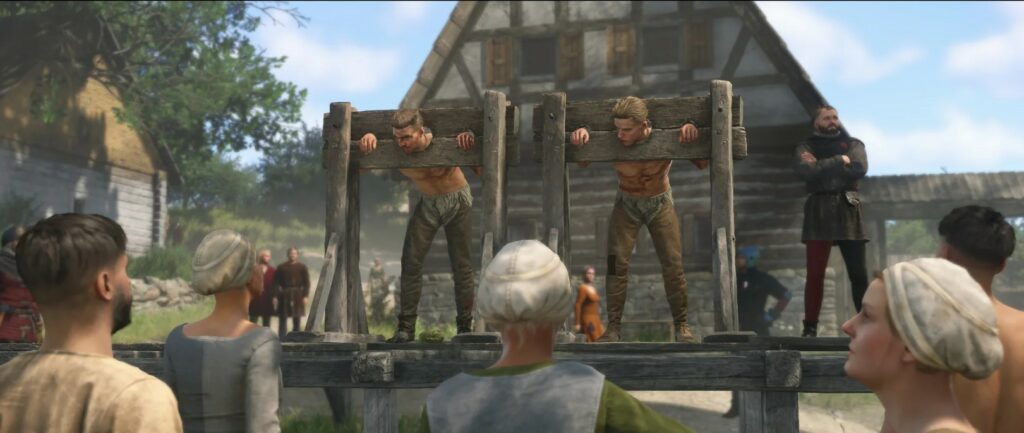 „Kingdom Come: Deliverance 2“ stopkadras: du vyrai įkalinti sląstuose, į juos žiūri kaimo bendruomenė